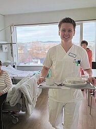 Ein Foto von Pflegefachmann Clemens Reiche, der ein Essenstablett trägt.